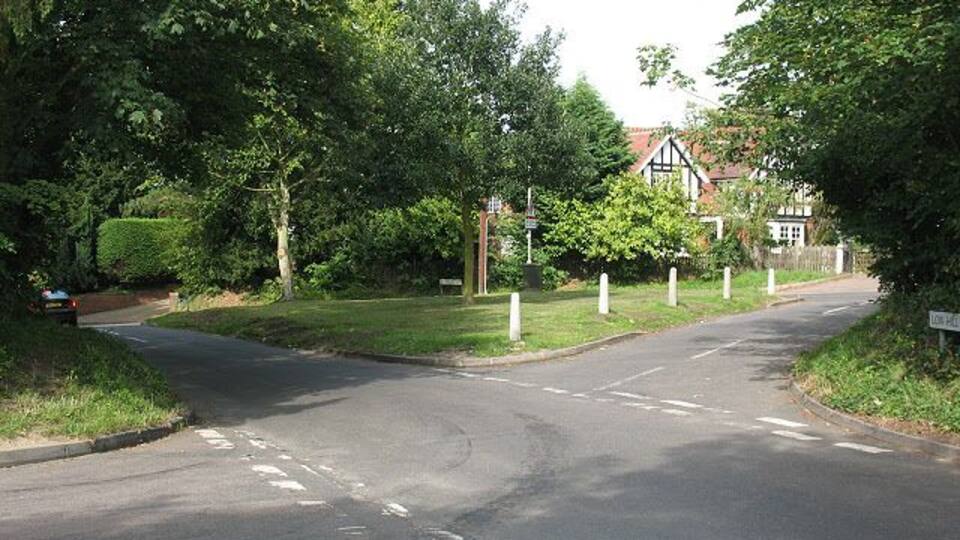 A quiet residential street with houses, trees, and a clear road.