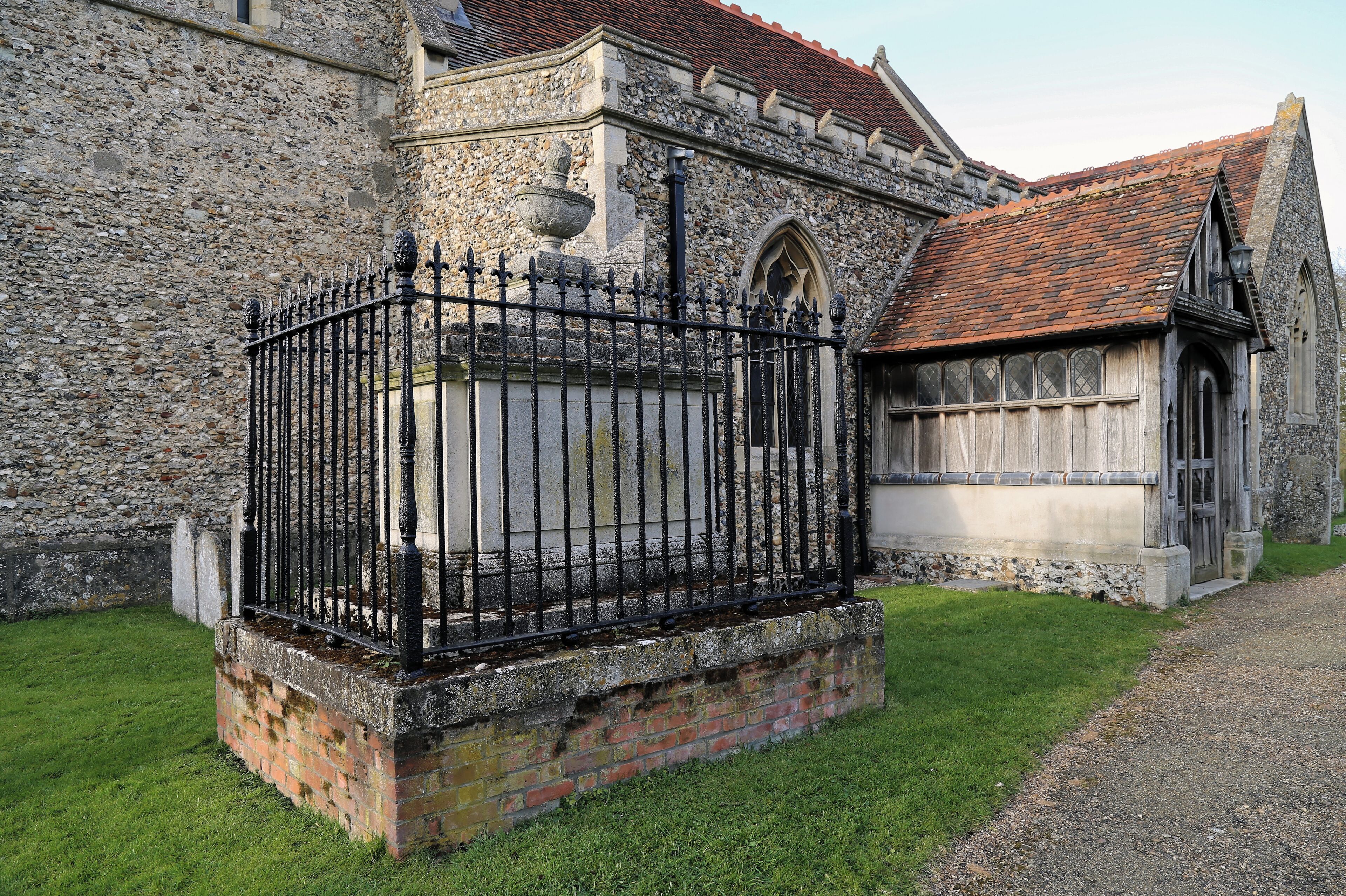A stone building with a brick base, a black iron fence, and a red-tiled roof.
