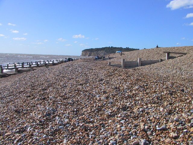 A pebble beach with a wooden fence and a cliff in the background.