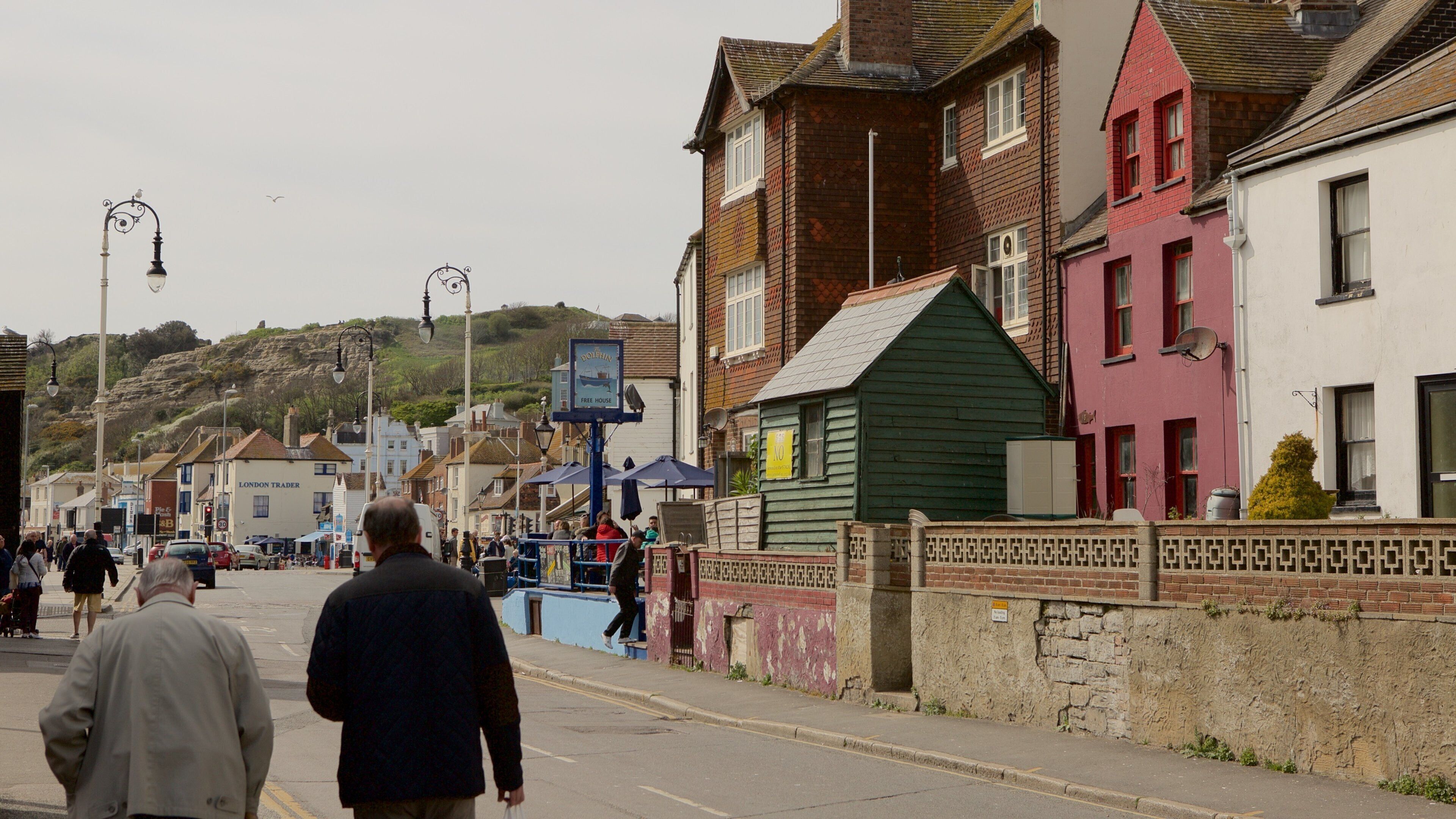 A street with people walking, buildings, and a hill in the background.