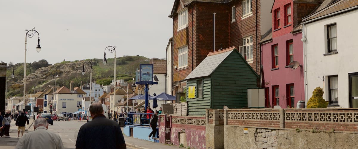 A street with people walking, buildings, and a hill in the background.