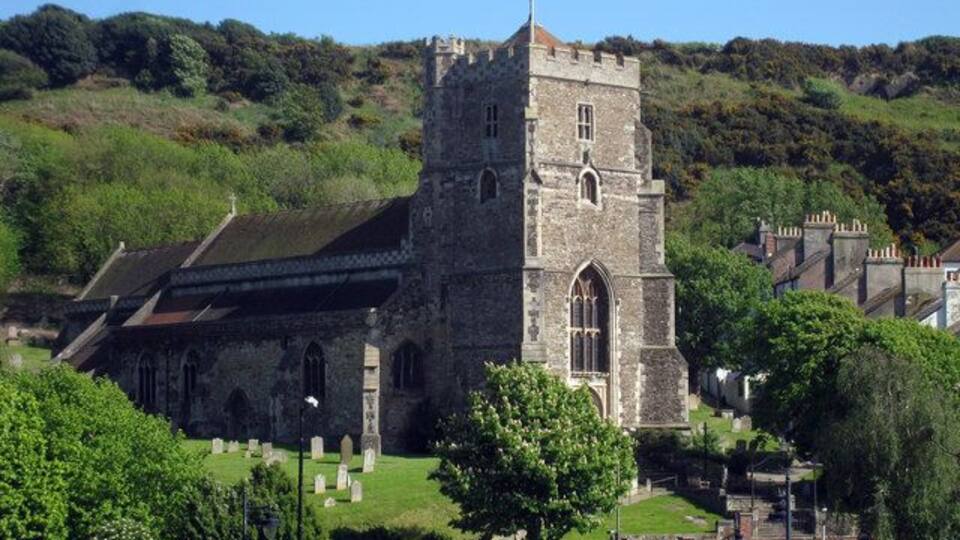 Una iglesia histórica con una torre destacada, rodeada de vegetación y un cementerio.