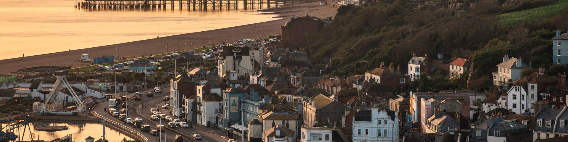 A coastal town with a pier extending into the sea, surrounded by buildings and hills.
