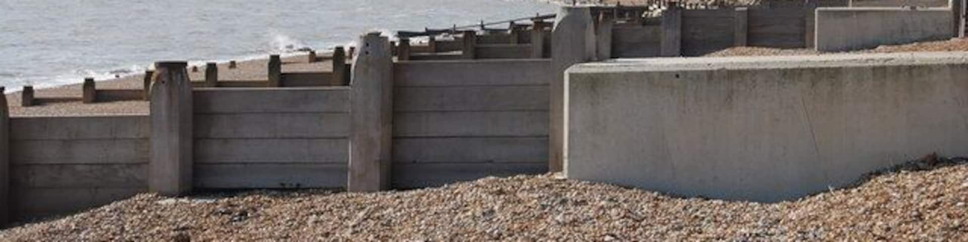 A rocky beach with a concrete sea wall and cliffs in the background.