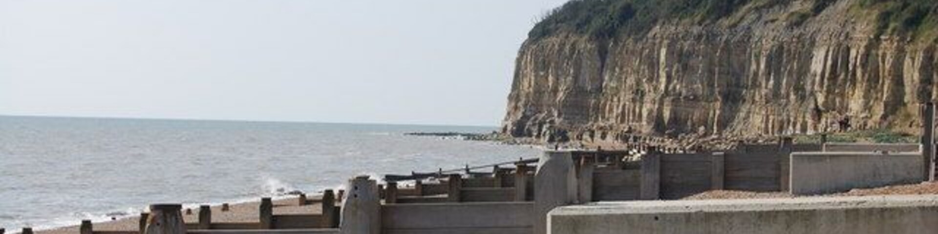 Una playa rocosa con un muro de contención de hormigón y acantilados al fondo.
