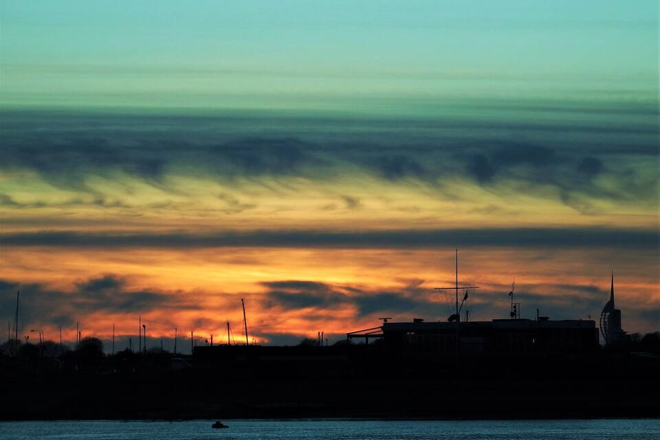 A sunset over a coastal city with silhouettes of buildings and a windmill.