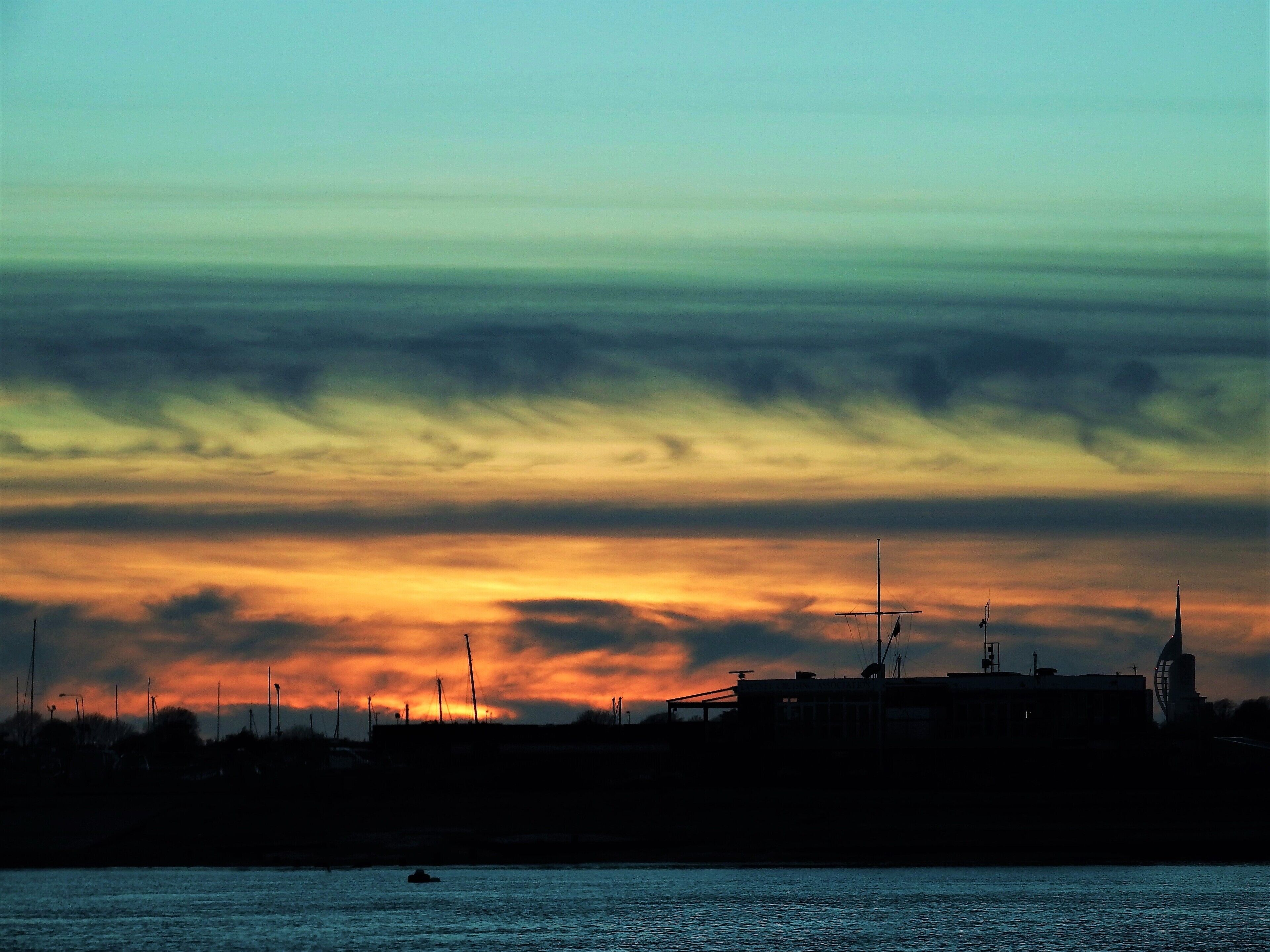 A sunset over a coastal city with silhouettes of buildings and a windmill.