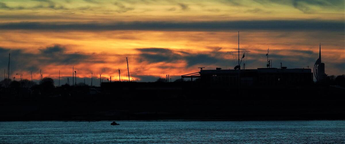 A sunset over a coastal city with silhouettes of buildings and a windmill.