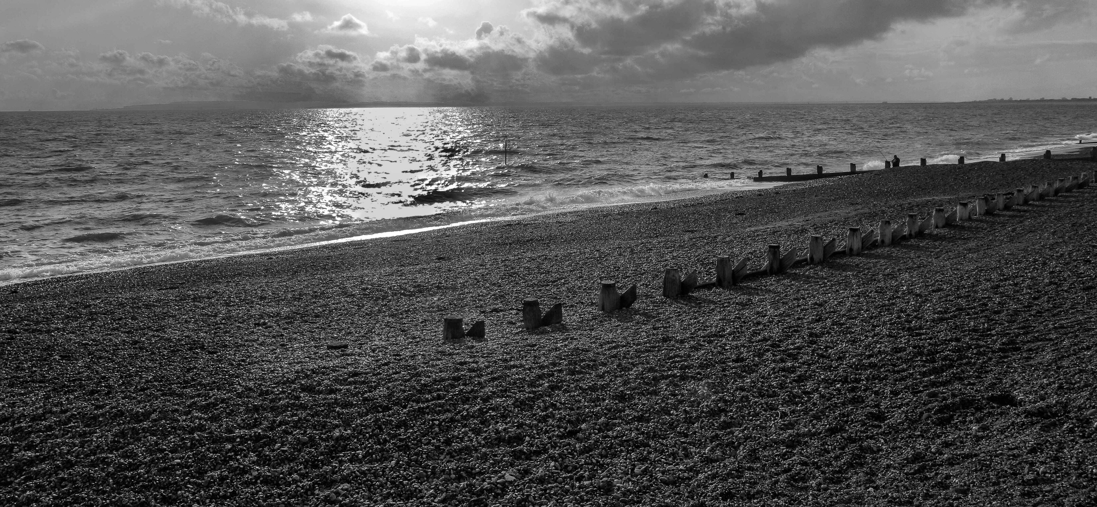 A pebbled beach with a row of wooden posts and a rough sea under a cloudy sky.
