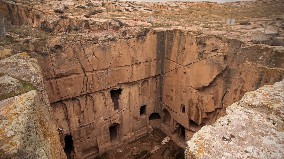A large rock formation with multiple caves and a fenced area.