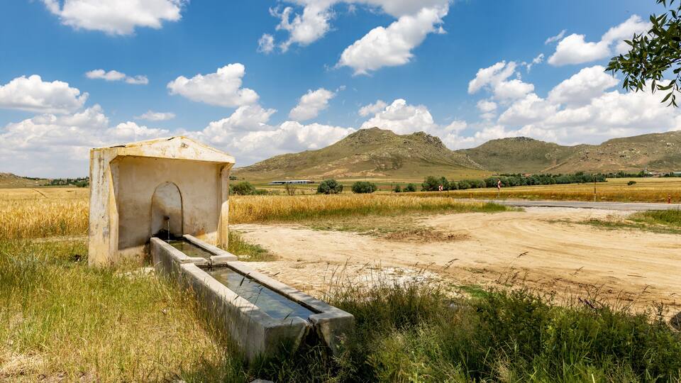 A concrete structure with a water channel in a rural landscape with mountains in the background.
