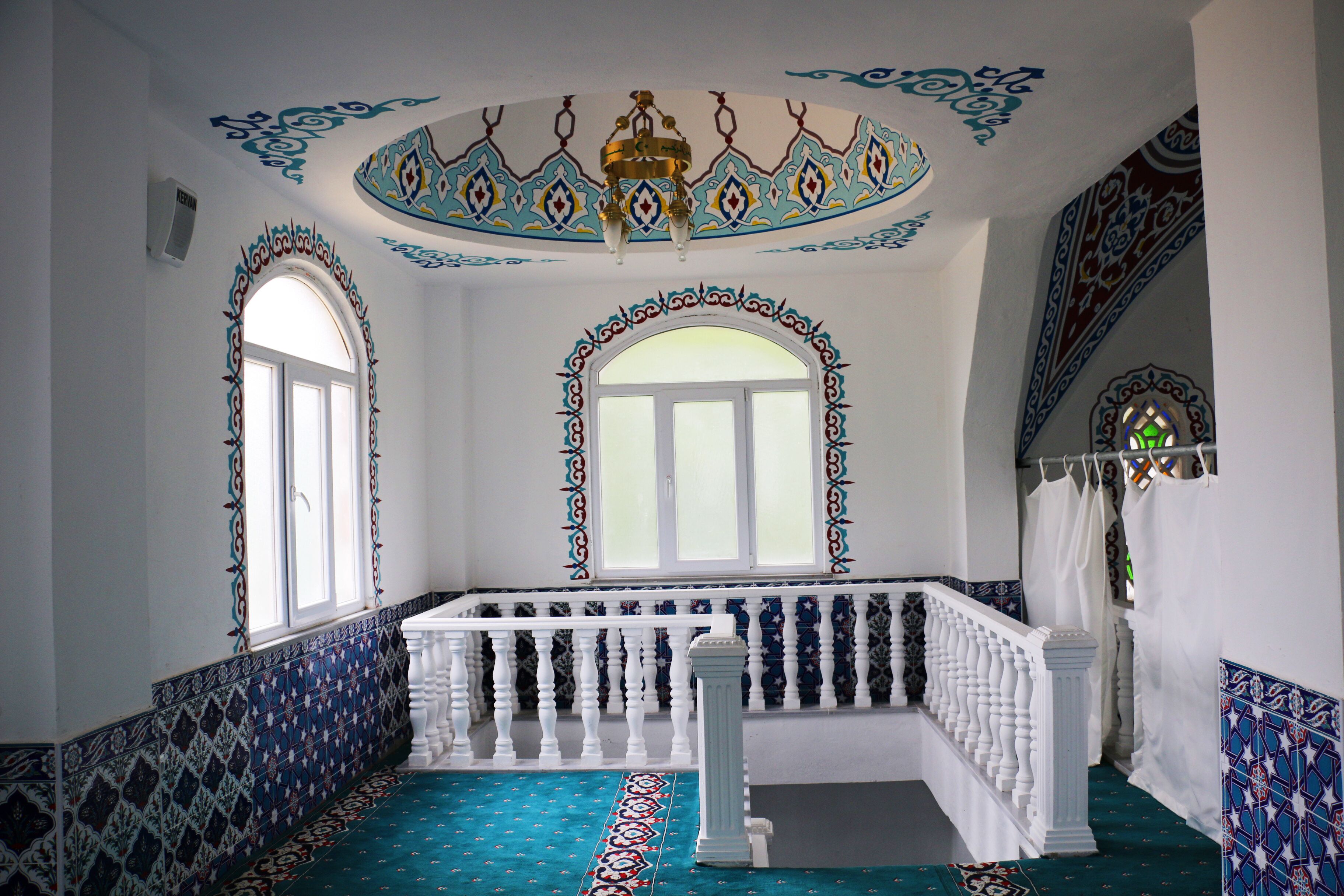 A room with ornate blue and white patterned walls, a white balcony railing, and a chandelier.