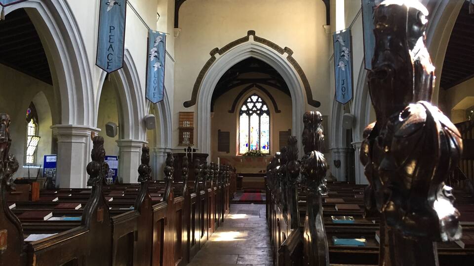 An interior of a church with wooden pews, a central aisle, and banners hanging from the ceiling.