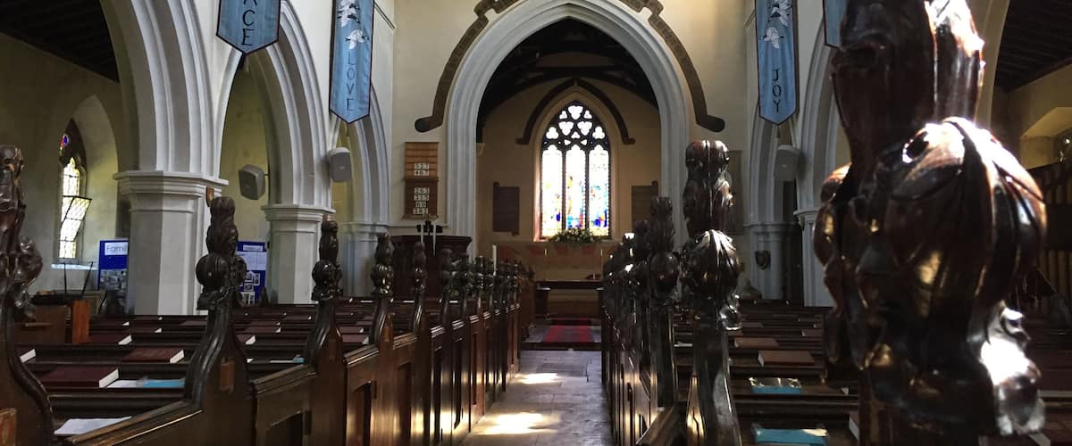 An interior of a church with wooden pews, a central aisle, and banners hanging from the ceiling.
