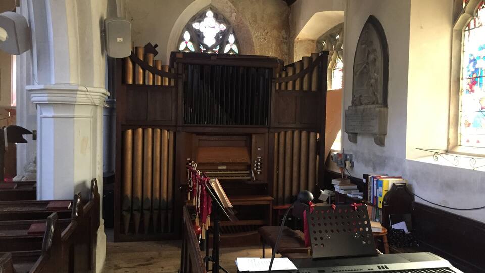 A church interior with wooden pews, a pipe organ, a keyboard, and stained glass windows.