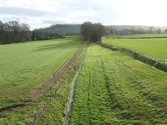 A rural landscape with a field, a fence, and a tree line.