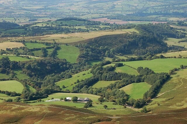 Rolling green hills, a small building, and a dense forest area.