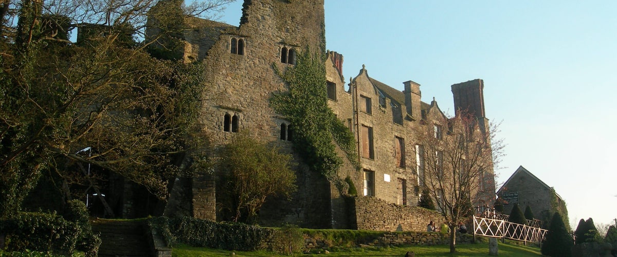 A historic stone castle with arched windows and a tower, surrounded by trees and a grassy area.