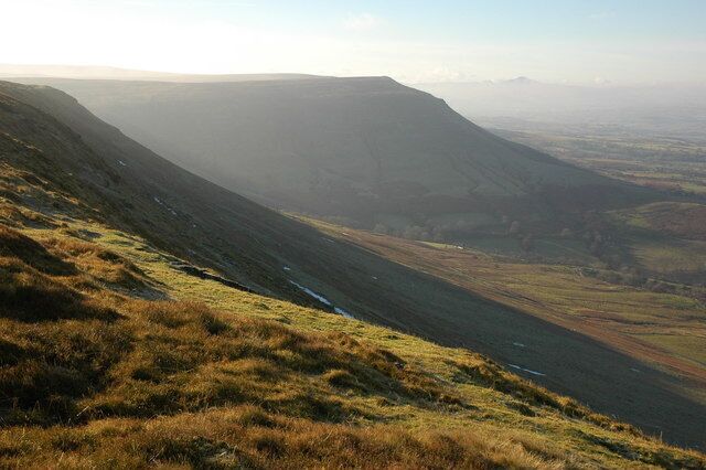A valley with a river, grassy slopes, and distant mountains.