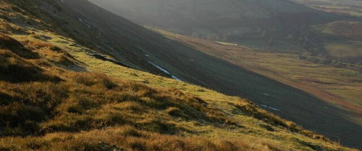 Un valle con un río, laderas cubiertas de hierba y montañas a lo lejos.