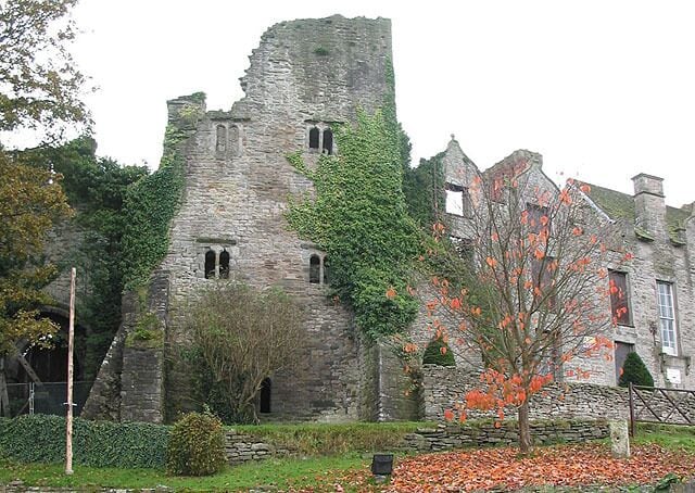 A historic stone castle with ivy-covered walls and a tree with orange leaves in front.