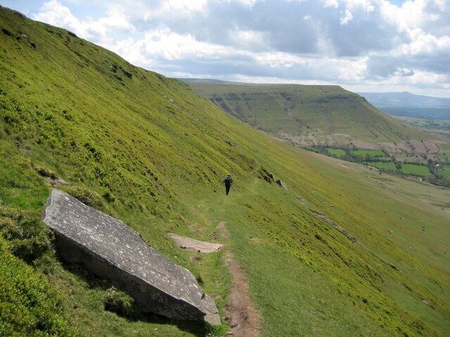 A grassy hillside with a stone slab and a trail.