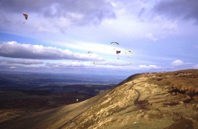 A landscape with a hilly terrain and several kites flying in the sky.