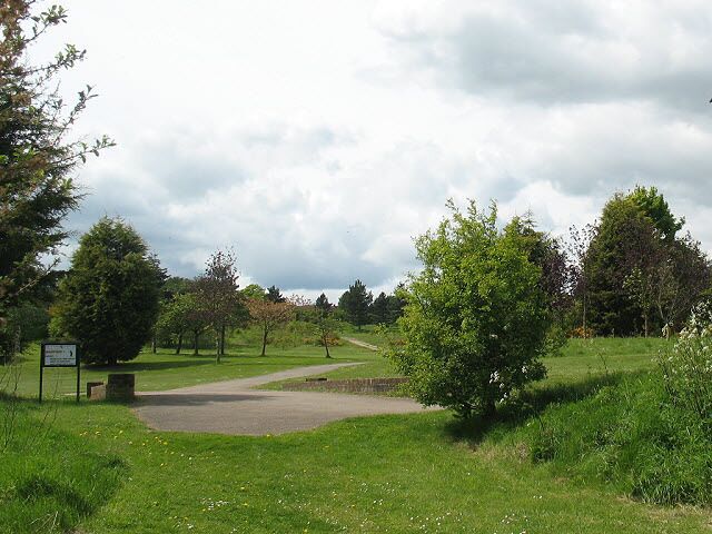 A park with a paved path, green grass, and trees.