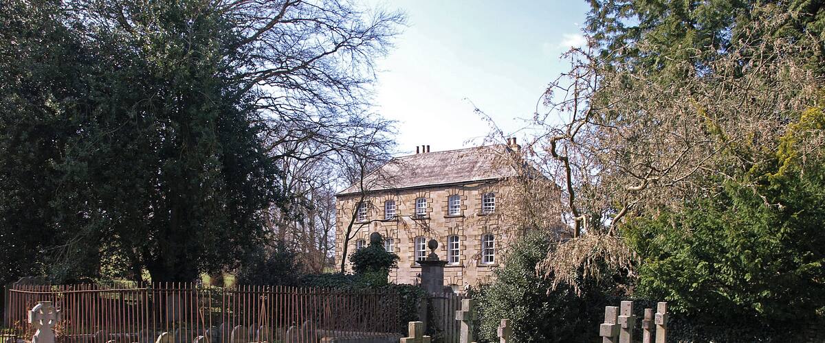 A cemetery with stone crosses and a historic building in the background.