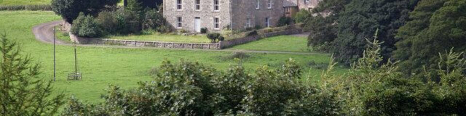 A large stone house surrounded by lush green fields and trees.