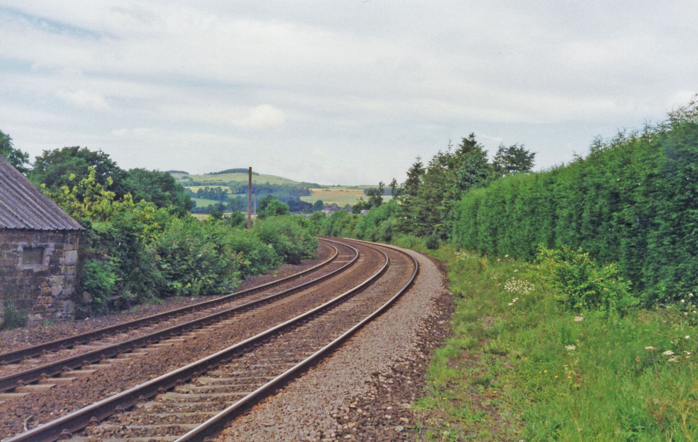 Railway tracks curving through a rural landscape with greenery and a stone building.