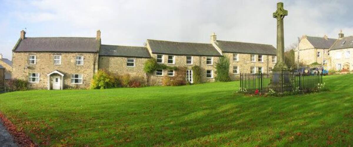 A stone building with a grassy lawn and a cross in the foreground.