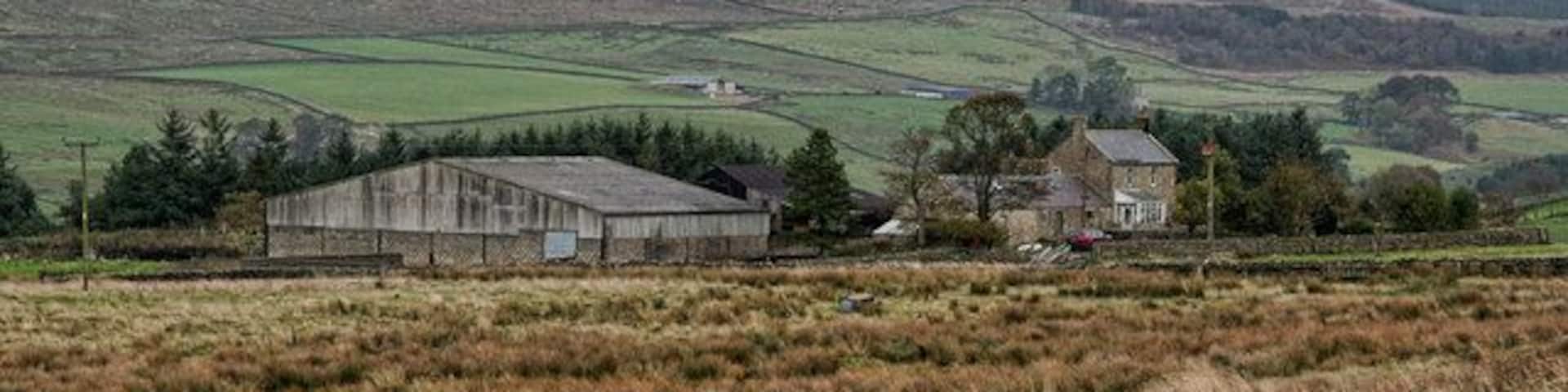 A rural landscape with a barn, a stone house, and rolling hills in the background.