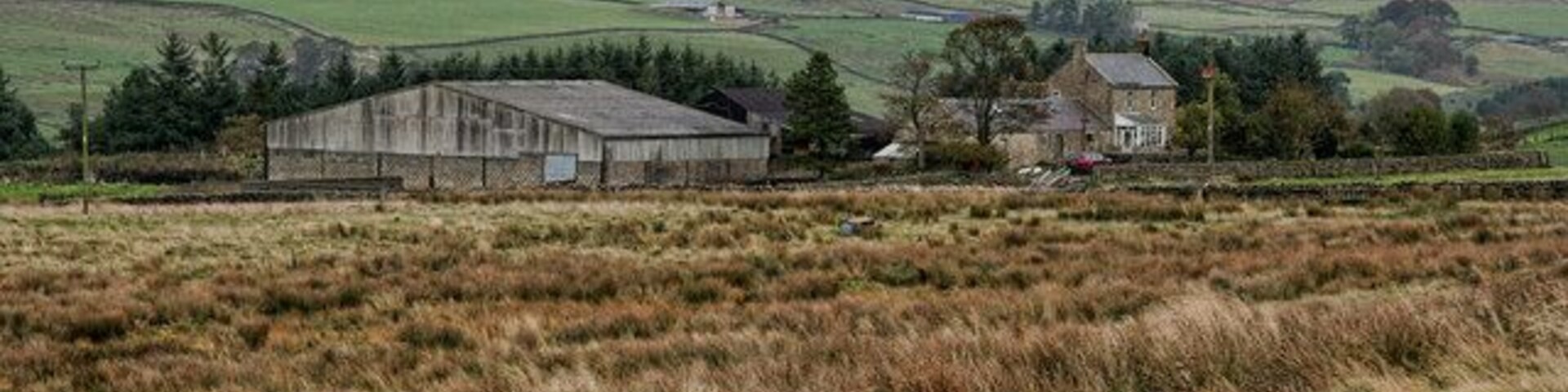 Paisagem rural com um celeiro, uma casa de pedra e colinas ondulantes ao fundo.