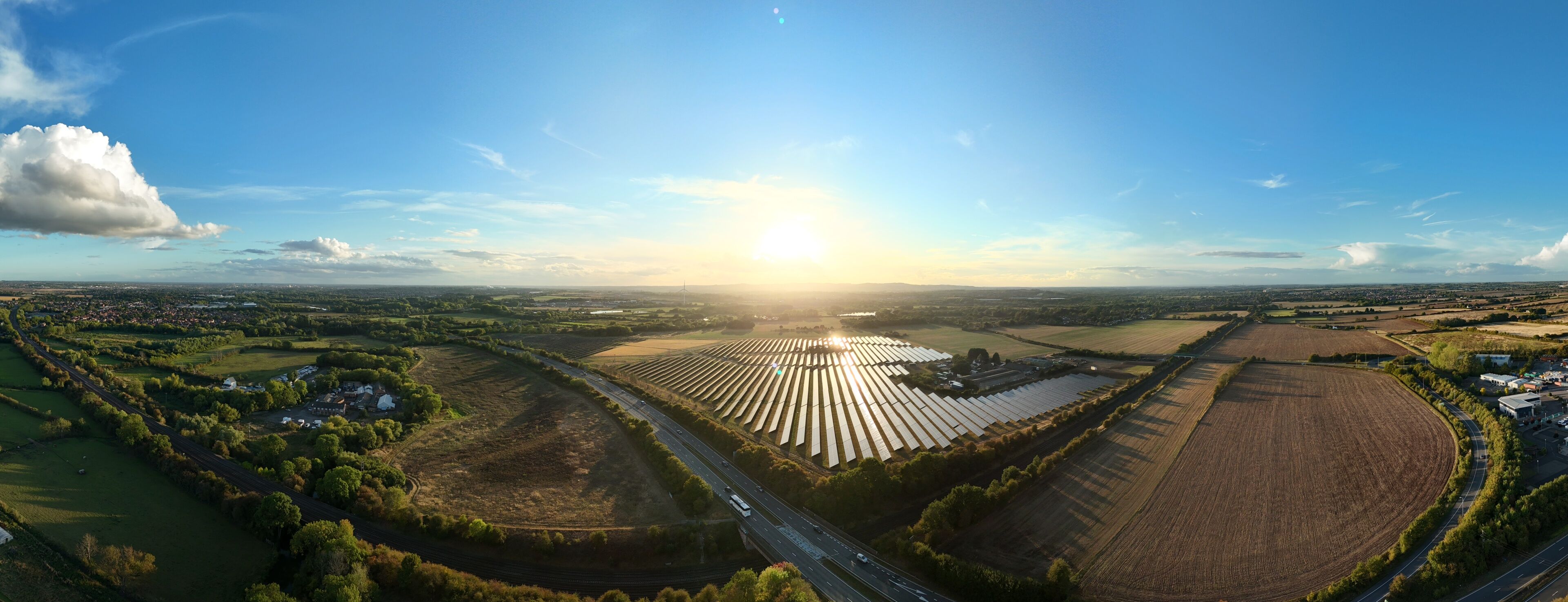 An aerial view of a rural landscape with a large solar farm, winding roads, and scattered houses.