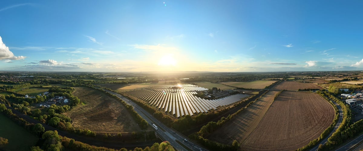 An aerial view of a rural landscape with a large solar farm, winding roads, and scattered houses.