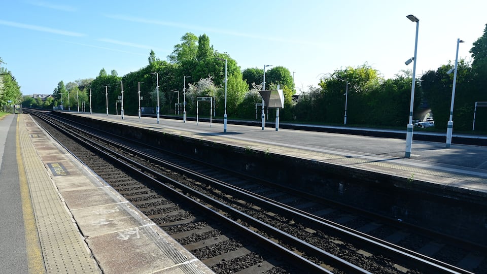 A train station platform with multiple tracks, overhead signage, and street lamps.