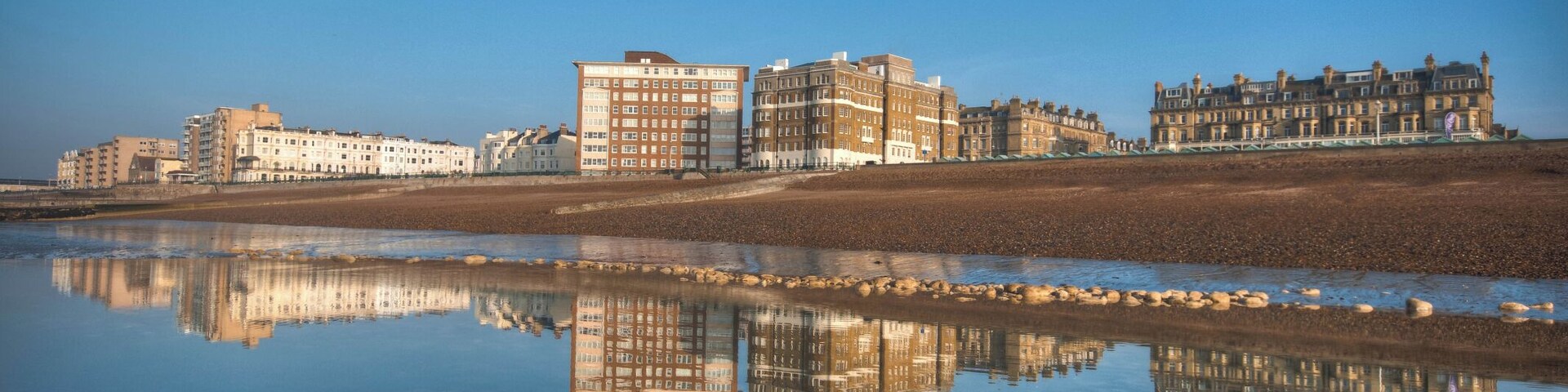 View of Hove promenade with reflection in sea at low tide against blue sky.