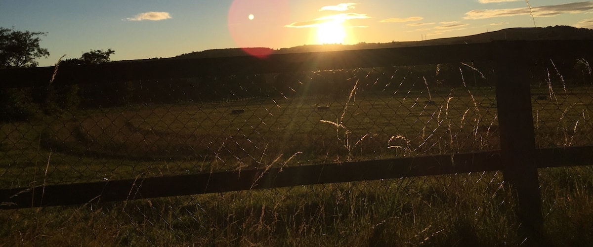A sunset over a field with a fence in the foreground.