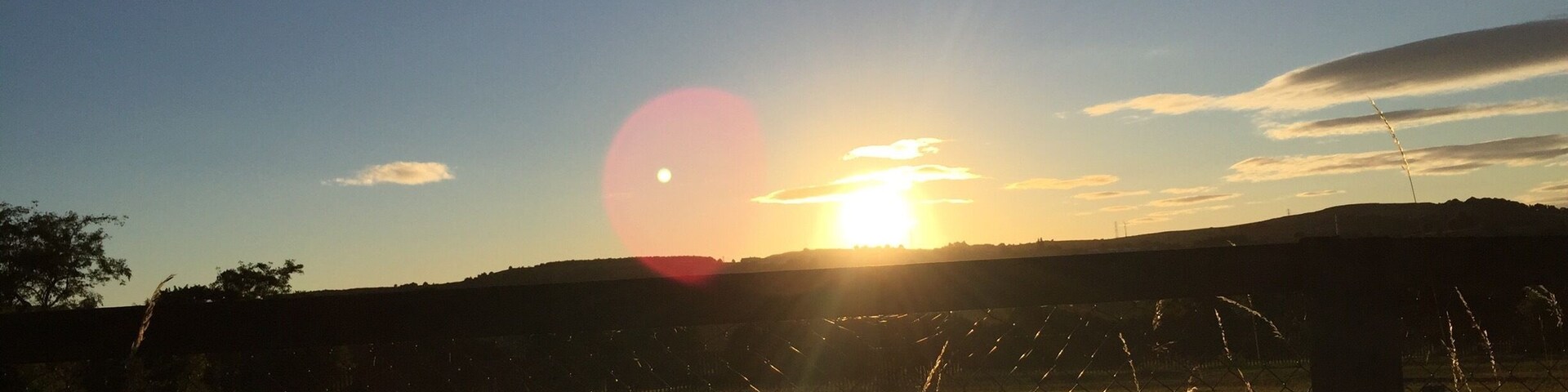 A sunset over a field with a fence in the foreground.