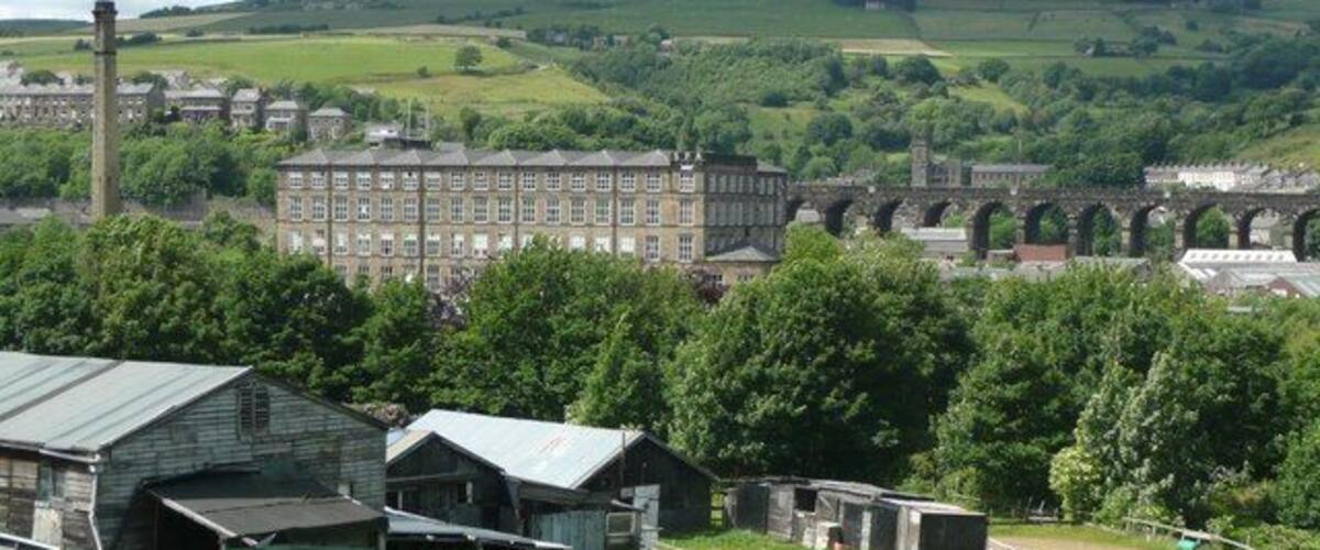 Un paysage rural avec un grand bâtiment, un pont et des champs verdoyants.