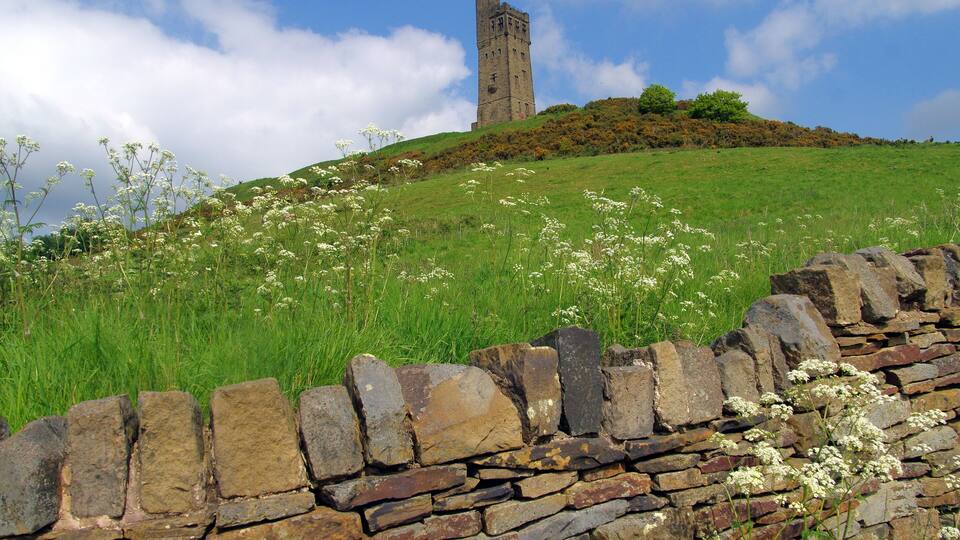 A stone wall, a grassy hill, and a tall tower.