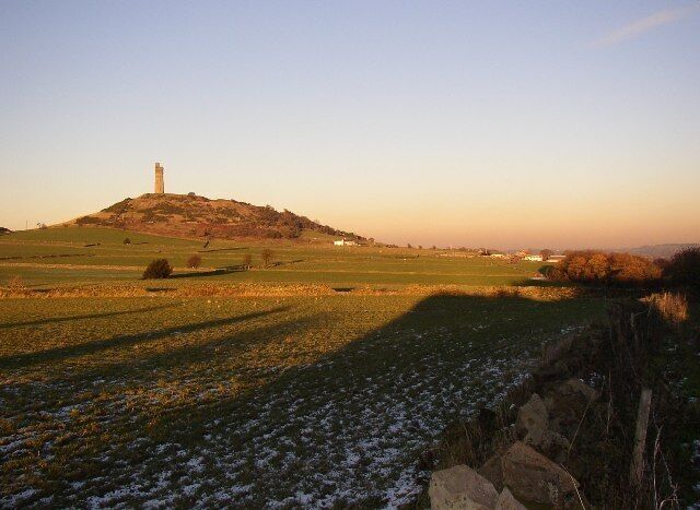 A grassy field with a hill and a tower in the distance.