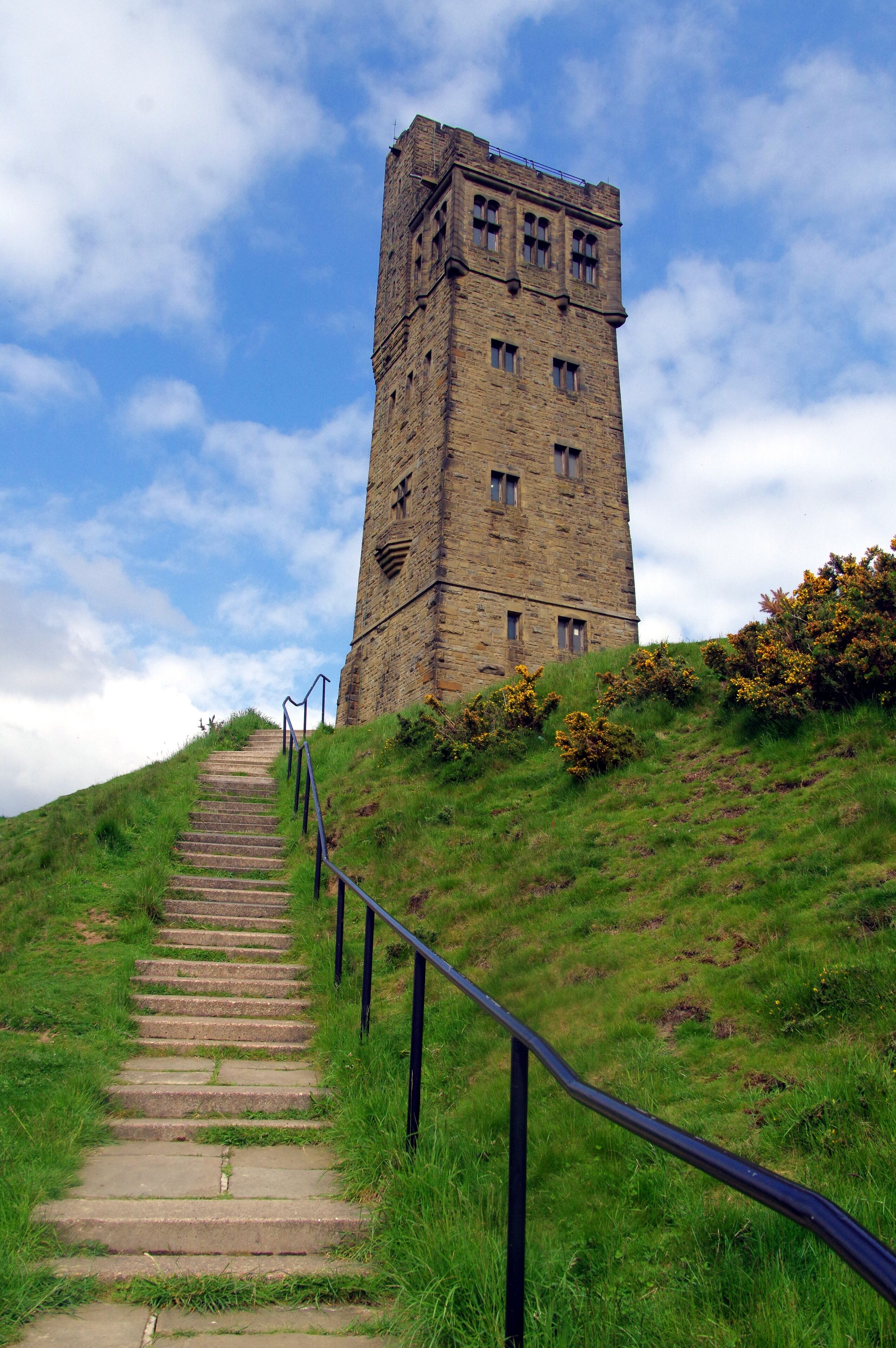 A stone tower with a staircase leading up to it, surrounded by grass and bushes.
