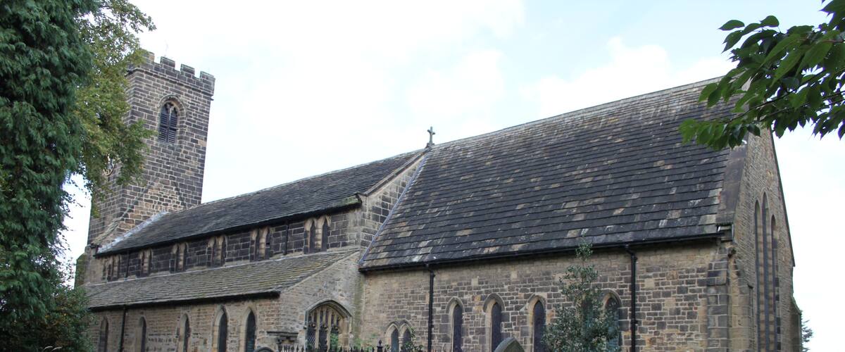 A historic church with a tall tower, stone walls, and a grassy cemetery with headstones.