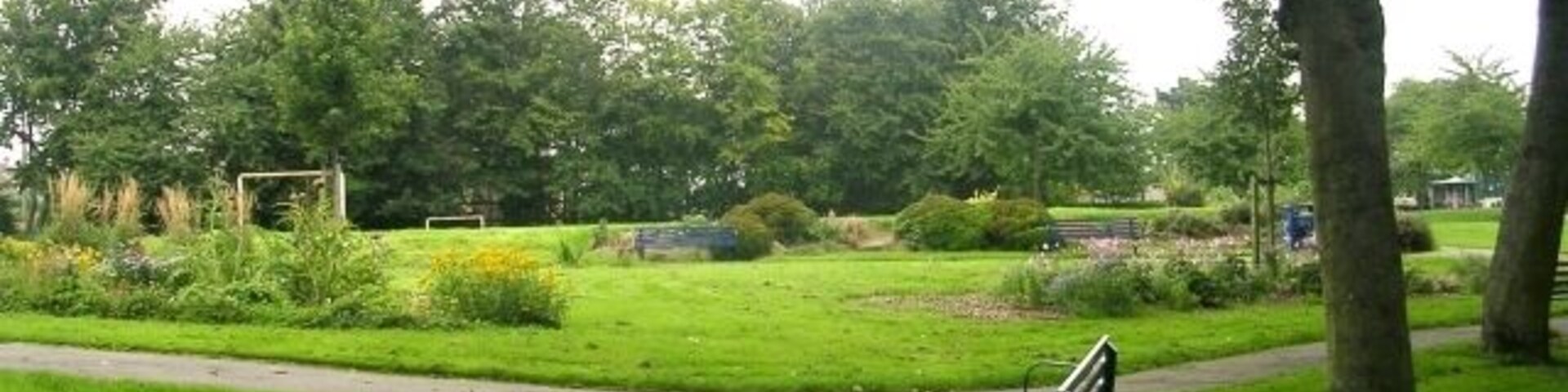 Un parque con un sendero pavimentado, bancos y abundante vegetación.