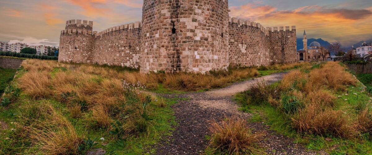 A medieval stone castle with a moat, surrounded by grass and a clear sky.