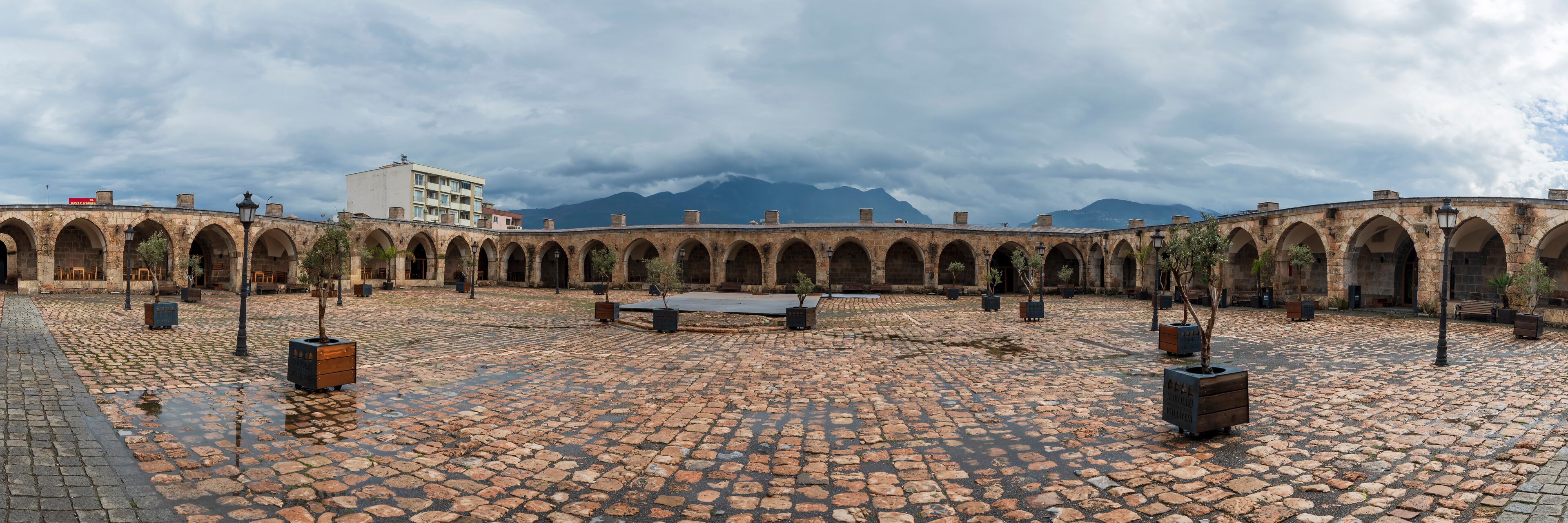 A courtyard with a cobblestone floor, arched walkways, and a building in the background.