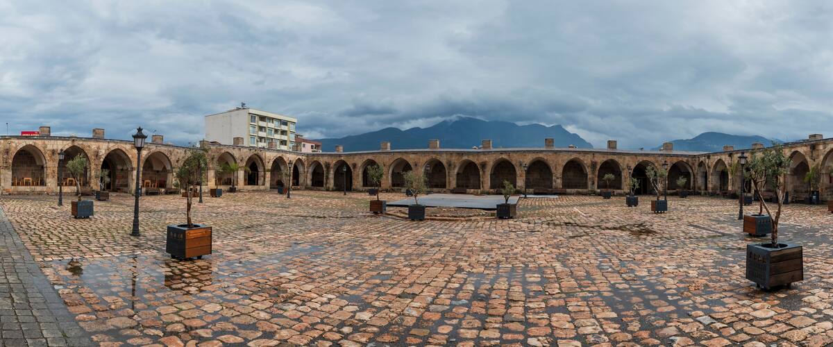 A courtyard with a cobblestone floor, arched walkways, and a building in the background.