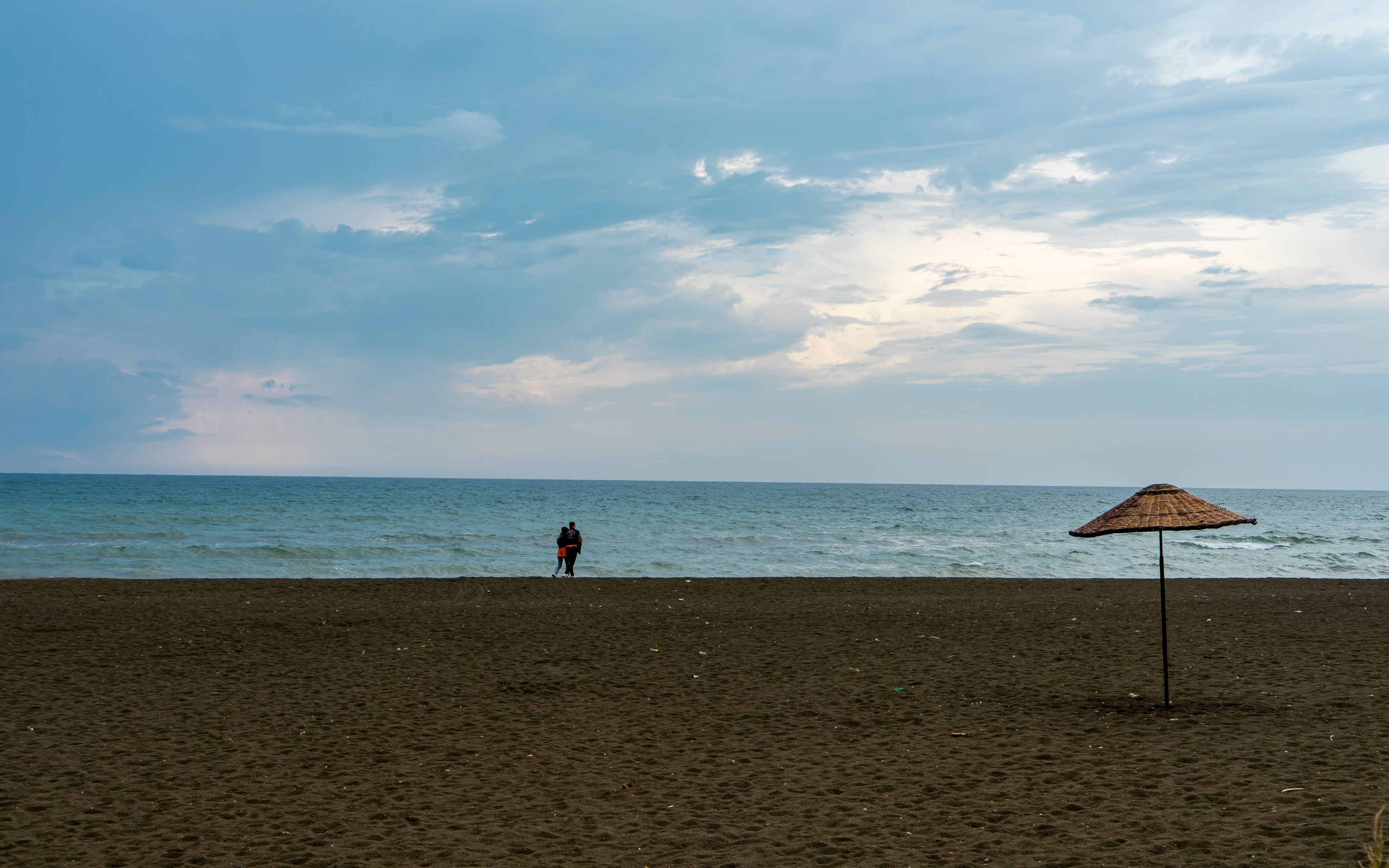 Couple walking and relaxing on sand. Travel vacation background concept on with single wicker umbrella in Samandağ, Antakya. Beautiful scene of beach, sea, blue sky and clouds. Copy space for text.